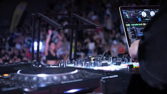 DJ mixing music at concert with audience in background and flashing lights