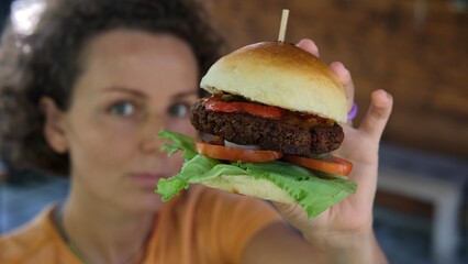 A young woman in a restaurant shows a vegetarian tasty hamburger with meat substitute. The concept of a healthy diet with the consumption of vegetables and the rejection of meat food.