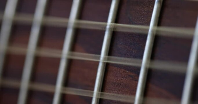 Closeup of acoustic guitar strings and the strings vibrate to reproduce melody of song