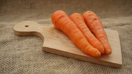 Flat lay fresh carrots on the cutting board with brown burlap background