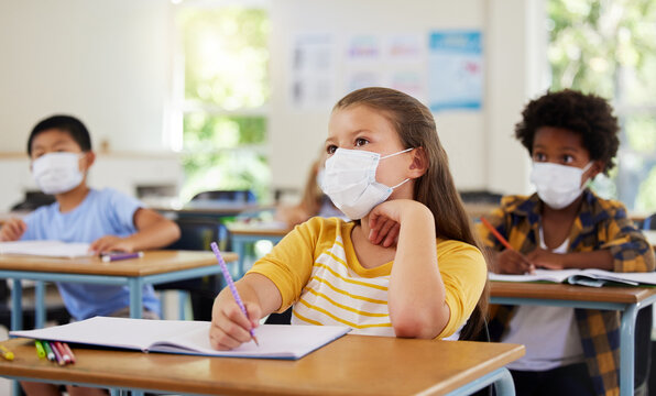 Focused Young Girl In School After Covid Pandemic, Sitting And Listening In Classroom While Taking Notes. Small Child Looking At Board, Learning And Thinking For Her Education With Other Students