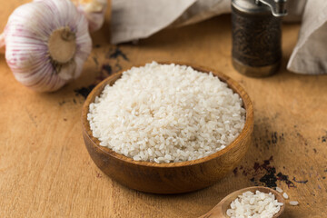 Fototapeta na wymiar Raw round white rice in a wooden bowl and in a wooden spoon on a wood background