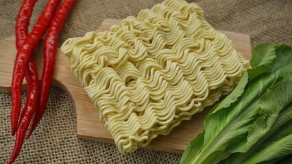 Crispy and dry instant square noodle. Uncook and unhealthy dried noodle on cutting board with mustard and chili. asian ramen instant noodles isolated on on burlap surface.