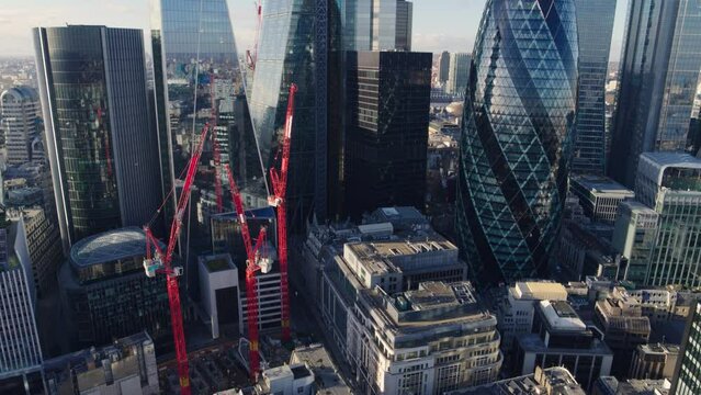 Descending and upward tilting aerial establishing shot over London financial district revealing a collection of iconic skyscrapers The Gherkin, The Cheesegrater, and The Scalpel under a clear blue sky