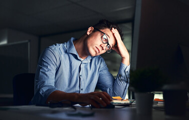 Tired, stressed businessman suffering from headache, working late night in the office. Serious, frustrated and overworked corporate male with headache staring at his screen in the dark.