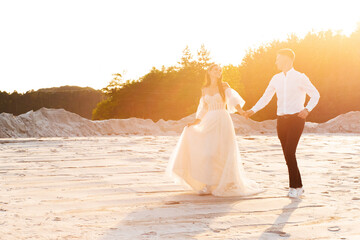 Fototapeta na wymiar Newlyweds in love, holding hands, run along the sandy beach at sunset.
