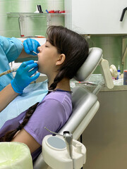 A girl sits in a dentist's chair, at a doctor's appointment, which she conducts an ultrasonic cleaning of her teeth.