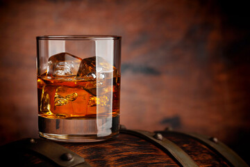 Glass of whiskey with ice cubes on the old barrel