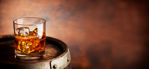 Glass of whiskey with ice cubes on the old barrel
