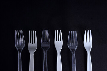 Various disposable plastic forks with copy space on dark background. Concept of recycling plastic and ecology.