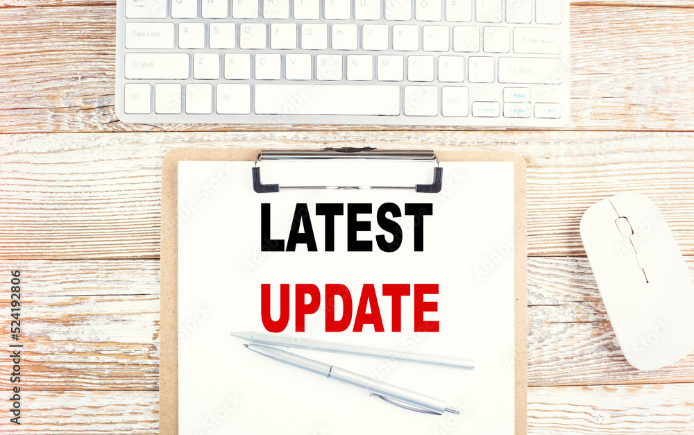 Poster latest update text on a clipboard with keyboard on wooden background
