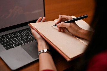 A businesswoman writing or taking notes something on her blank notebook at her office desk.