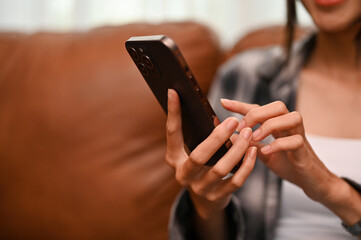 Beautiful Asian woman using smartphone while relaxing in her living room. cropped image