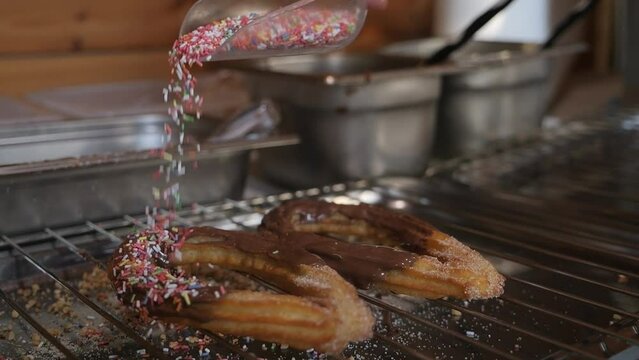 Fresh chocolate covered churros with multicolor sprinkles being drizzled on top