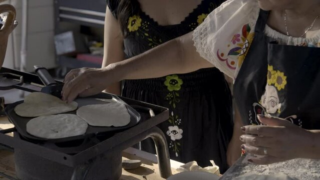 Indigenous mom and daughter put masa on a griddle. 