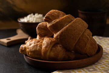 Cozy breakfast with croissants, cottage cheese and milk on a dark background with textiles, wooden...