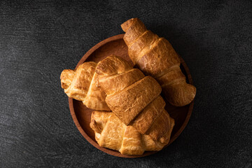 Close-up of golden croissants in a wooden plate on a dark background. French pastries. Rustic...