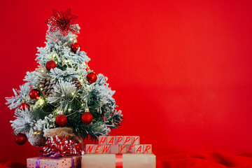 Small decorated Christmas tree with presents and happy new year message. Copy space on red background