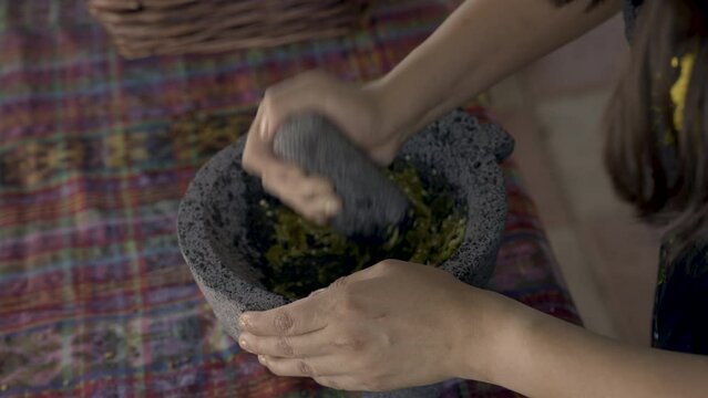 Indigenous woman crushes chiles with a molcajete. 