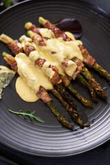baked aspargus covered with bacon on a black ceramic plate