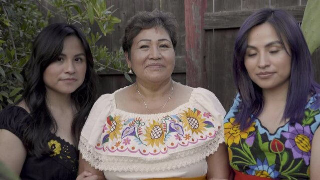 Indigenous mother and daughters pose for the camera in their outdoor garden. 