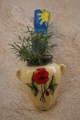 closeup of a colorful ceramic vase with flowers on the wall with an unusual painted water bottle can