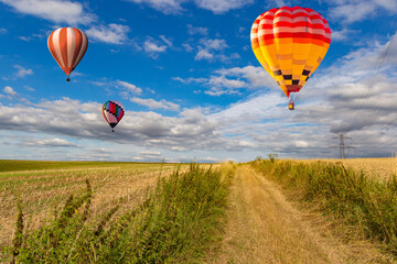 Fototapeta premium Multicolored hot air balloons fly in blue sky with white clouds over green field.