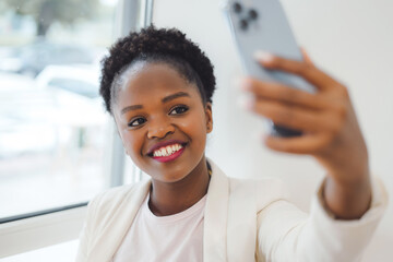 Naklejka premium Beautiful african woman taking selfie while resting in a coffee shop. Education internet technology. Beauty portrait.