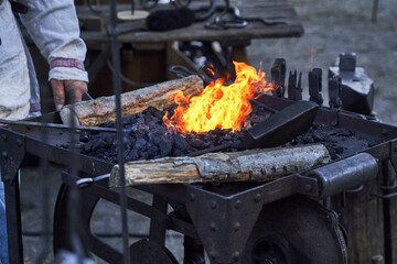 Blazing bright fire in the iron forge basin of the blacksmith filled with charcoal, wood and tools