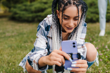 Fototapeta The girl with the afro pigtails arranges the phone in order to film herself in a tik tok video. Active life on the Internet. Followers drop. obraz