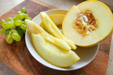 sliced melon with seeds on a white plate, green grapes on a wooden board, the concept of fresh fruit and healthy eating