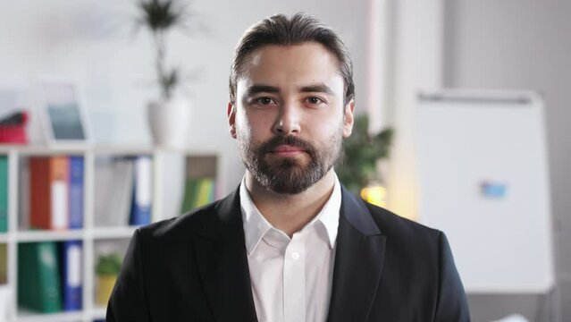 Portrait of caucasian male employee wearing black formal suit with neutral facial expression posing indoors. Blur background of bright modern business center.