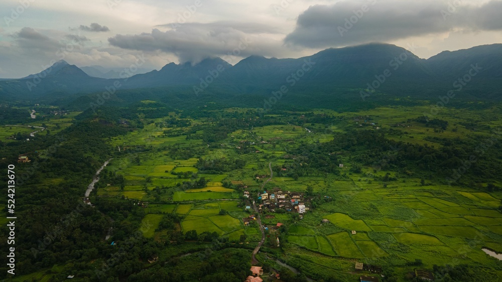 Wall mural aerial view of beautiful green land and the mountains in the background on a cloudy day