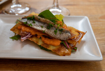 Spanish food, one tapas small piece of roasted bread cracker with vegetables puree and smoked sardine fish
