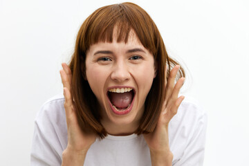 a close horizontal studio photo of a red-haired woman screaming loudly clutching her head from shock.