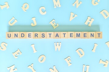 Understatement figure of speech concept in English grammar class lesson. Wooden blocks typography flat lay in blue background.