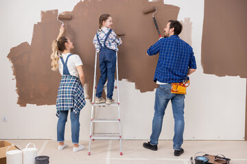 Three persons from the back, looking at each other and painting the wall in brown color. A little...