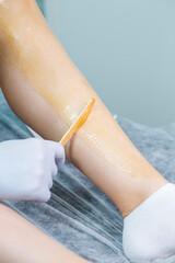 Spa Concepts. Close-up of Beautician Preparing for Wax Depilation of Woman Legs By Applying Liquid Wax With Spatula on Female Legs.