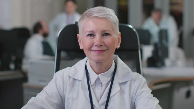 Portrait of mature woman doctor smiling at camera sitting in clinic office