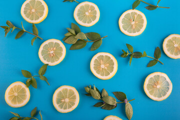 Lemon slices and green miny leaves pattern on vibrant turquoise color background. Minimal flat lay food texture on grained background
