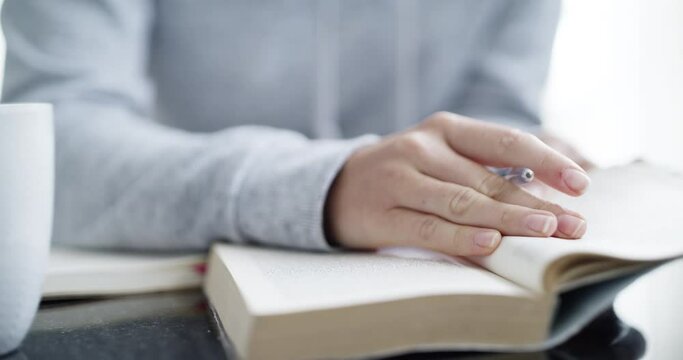 Closeup of a student hands writing notes from a textbook while studying. Person researching, listing information in a notebook while brainstorming and planning, preparing for an exam, test or finals