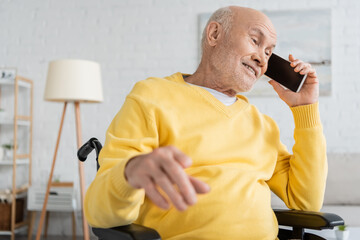 Positive senior man talking on smartphone in wheelchair at home.