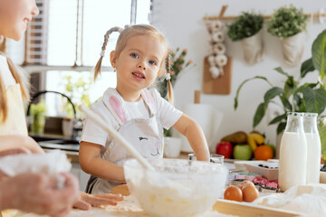 Adorable happy preschooler kid wearing funny apron helping mother and granny in modern light kitchen. Baking cooking homemade pizza bread preparing surprise for dinner.