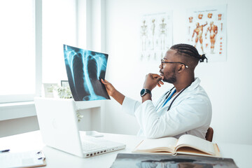 Obraz premium Afrian American adult male doctor looking at x-ray. Doctor examining a lung radiography. Doctor examining chest x-ray film of patient at hospital. 