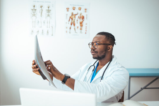 Healthcare, technology, rontgen, people and medicine concept - smiling male doctor in white coat with laptop computer looking at x-ray in medical office. Male doctor reviews x-ray