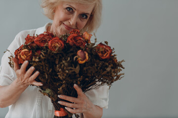 Positive smiling elderly woman hold in hands rose flowers bouquet