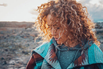 Side portrait of attractive woman with blonde coloured long curly hair looking down and enjoying outdoors nature feeling. Travel adult female people concept lifestyle with desert in background