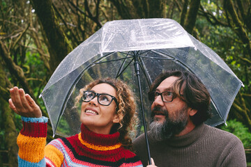 Young mature couple man and woman checking weather under umbrella in rainy day. Outdoor leisure activity people in the park in autumn or winter time. Rain and bad forecast condition. Love and friends