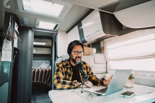 One modern man work with microphone and laptop to record a podcast inside a camper van house and alternative office. Concept of people and digital nomad lifestyle. Travel job everywhere connected