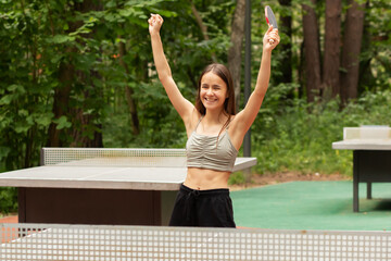 ping pong winner, happy girl with a racket raised her hands up, rejoices at the victory, sports success